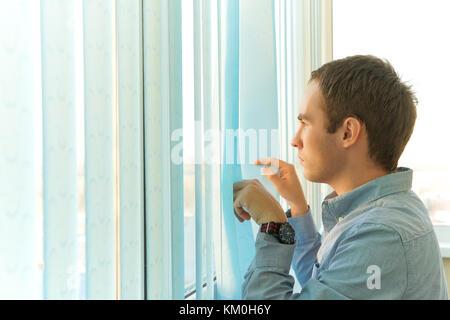 Successful businessman with thinking about something while standing near window with a venetian blinds, thoughtful men entrepreneur dressed in the blu Stock Photo