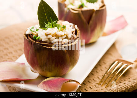 Stuffed artichokes with risotto on elegant table with golden fork Stock Photo