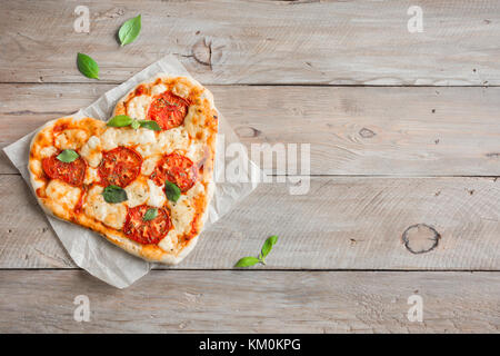 Heart shaped pizza Margherita over wooden background with copy space. Pizza with tomatoes, mozzarella cheese and basil for Valentine's day. Stock Photo