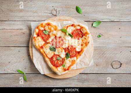 Heart shaped pizza Margherita over wooden background with copy space. Pizza with tomatoes, mozzarella cheese and basil for Valentine's day. Stock Photo