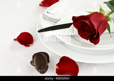 Beautiful long stem red rose across an empty dinner plate setting with chocolate candy. Shallow depth of field. Stock Photo