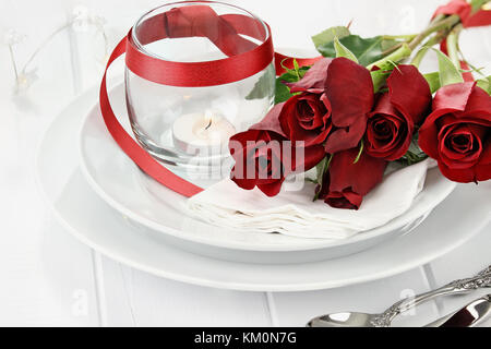 Romantic candlelite table setting with long stem red roses and candles in the background. Shallow depth of field with selective focus on roses. Stock Photo