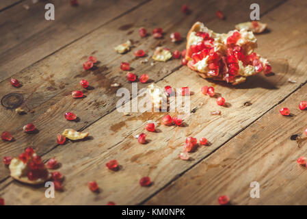 Falling down ripe pomegranate with cracks and splashes of juice and seeds wooden vintage background. Stock Photo