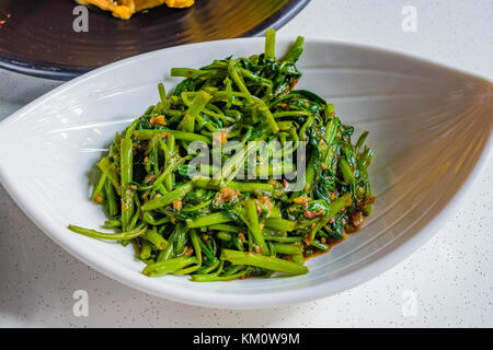 Chinese Fried Water Spinach with spicy chili garlic and soy sauce on white plate, in Singapore called Sambal Kangkong Stock Photo