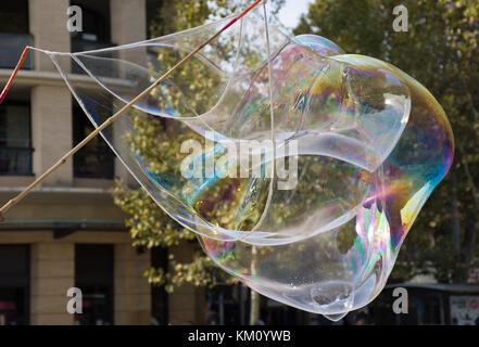 Close up of a gigantic iridescent bubble with turquoise, fuchsia and gold. Bamboo sticks and string to make the bubble are seen. Shallow depth of fiel Stock Photo