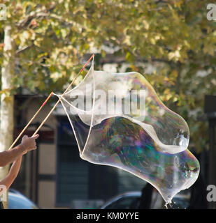 A huge iridescent bubble made with soap, water and air by two people holding bamboo sticks. Only their arms are shown. Stock Photo