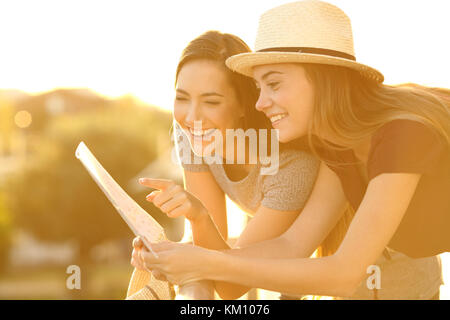 Two funny tourists reading a paper map in an hotel balcony on holidays at sunset Stock Photo