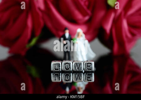 Miniature scale model wedding couple with the word love on beads and rose bouquet Stock Photo