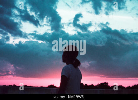Silhouette of woman looking out at the cloudy sunset sky Stock Photo