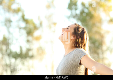 Side view portrait of a woman breathing fresh air outdoors in summer with trees and sky in the background Stock Photo
