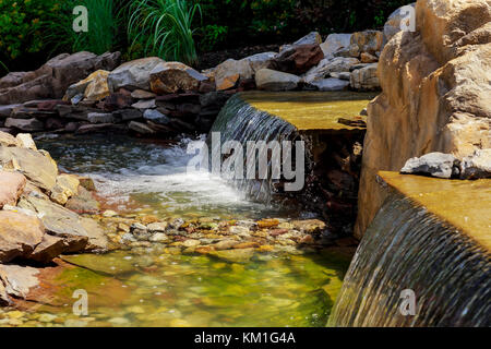 Waterfall at the source. Small Modern fountain in the park on the summer territory. A small fountain in the middle of a small artificial lake Stock Photo