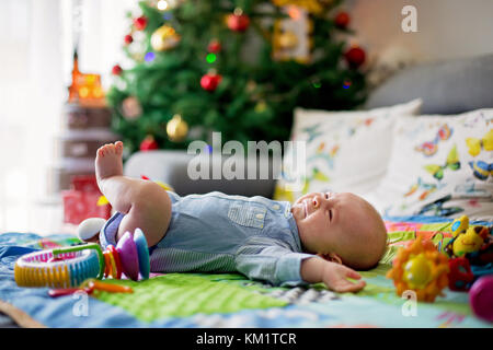 Three months old baby boy, crying at home on a colorful activity blanket, toys and different activity around him