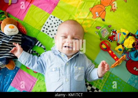 Three months old baby boy, crying at home on a colorful activity blanket, toys and different activity around him