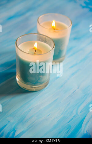 Two lit up candles on blue surface. Stock Photo