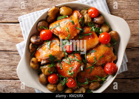 Fried chicken with chestnuts, greens and tomatoes close-up in a bowl on the table. horizontal top view from above Stock Photo