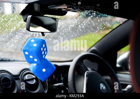 Two large, kitsch, blue, furry or fuzzy dice associated with boy racers in the seventies and eighties hang from the interior rear view mirror of a car Stock Photo
