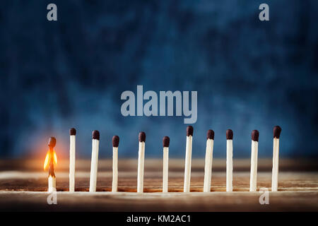 row of matches, one is lit. One burning match to the left of the rest. Concept of the idea. Top place for text Stock Photo
