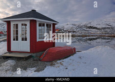 Red painted rowboat and wooden cabin with black roof and white closed door and window on Hjertholmen islet-E.boundary of the fishing port-mounts Lodin Stock Photo