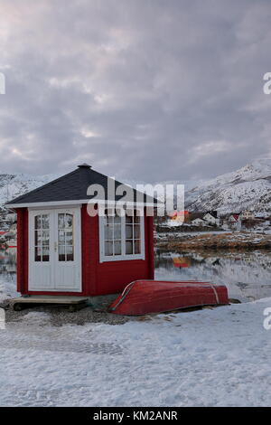 Red painted rowboat and wooden cabin with black roof and white closed door and window on Hjertholmen islet-E.boundary of the fishing port-mounts Lodin Stock Photo