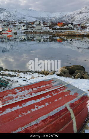 Red painted wooden rowboat aground on the snowy floor of Hjertholmen islet breakwater-east boundary of the fishing port-mounts Lodingsaksla in back. L Stock Photo