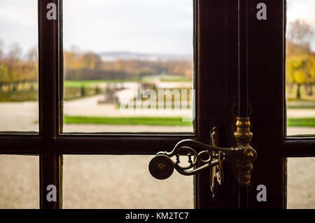 Close-up view of an espagnolette type locking device on a wooden casement window in a french castle with a blurry landscape background showing a frenc Stock Photo