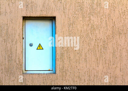 White hinged power supply box on the wall. Electrical panel with fuses and switches. Voltage control in switchboard with sign electrical hazards. Stock Photo