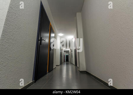 Narrow white corridor with many doors in an apartment building Stock Photo