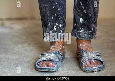 Feet of a construction worker in old dirty clothes and shoes Stock Photo