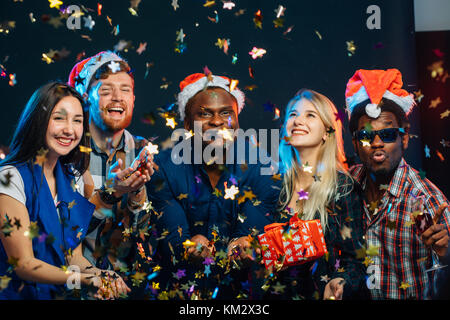 friends at New Year's party, wearing santa hats, dancing and blowing confetti Stock Photo