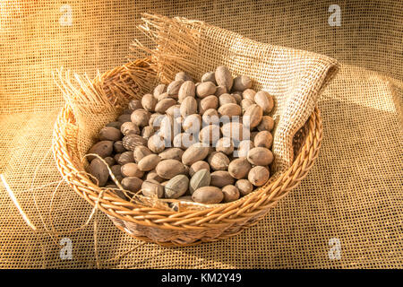 Pecans in basket wrapped with burlap textile with morning sunlight from window. Stock Photo
