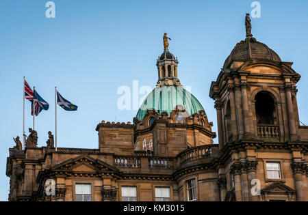 Roof of Bank of Scotland headquarters, The Mound, Edinburgh, UK, lit up at dusk with copper dome and flags flying against blue sky Stock Photo