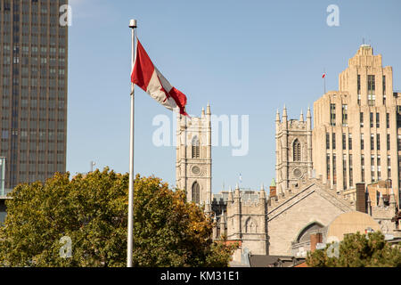 Montreal, Quebec, Canada skyline with towers of Basilica of Notre Dame next to modern high rise buildings and Canadian flag on flagpole against blue s Stock Photo