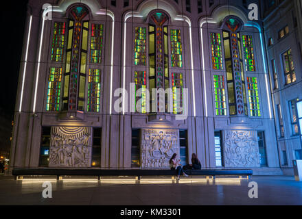 BERLIN, GERMANY - AUGUST 26, 2017; Two young women in dark of night sit on bench below beautifully designed and lit Freidrichestrasse Theater Stock Photo