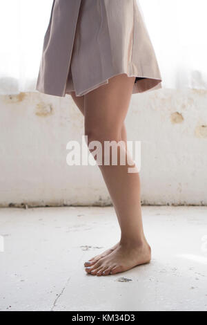 Side view of a barefooted woman standing by the window Stock Photo