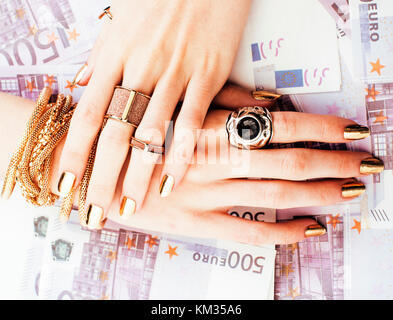 hands of rich woman with golden manicure and many jewelry rings on cash euros Stock Photo