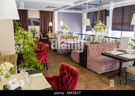 Interior of restaurant with brown sofas, red velvet armchairs and flower decorations Stock Photo