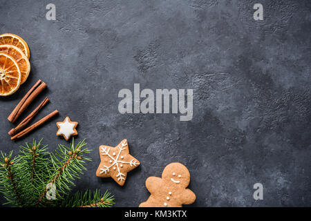 Christmas background with fir tree branches, cinnamon, gingerbread cookies and dried orange rings. Dark stone or textured chalkboard background. Copy  Stock Photo