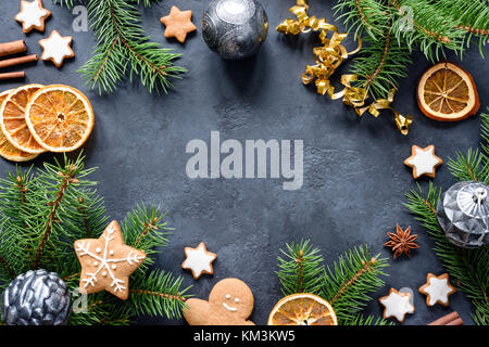 Christmas or New Year frame with fir tree branches, gingerbread cookies, spices, dried orange rings and Christmas toys on stone background. Copy space Stock Photo