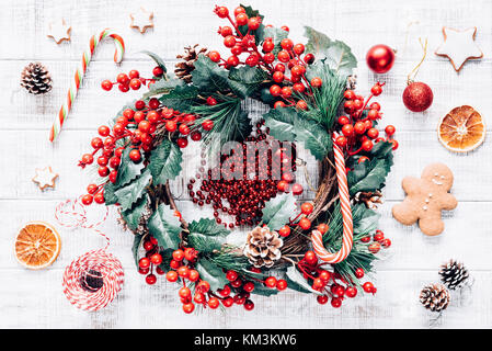 Christmas winter wreath, candy canes, Christmas tree decorations and gingerbread cookies on old white wooden background. Wallpaper, background or holi Stock Photo