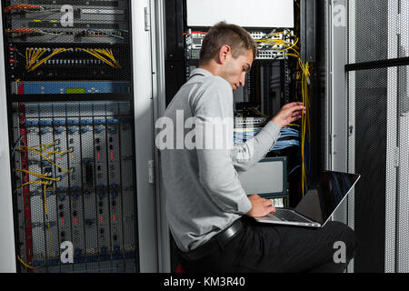 Portrait of modern young man holding laptop standing in server room working with supercomputer Stock Photo
