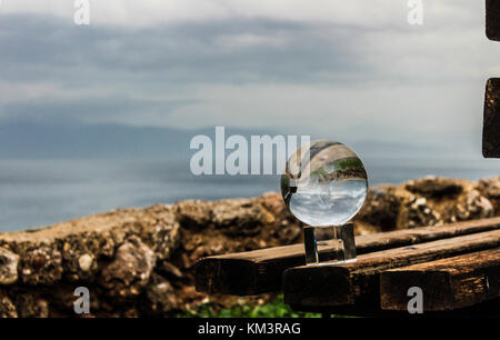 crystal ball on a bench on the edge of a cliff with colorful scenery on the background sea and clouds  greece december Stock Photo