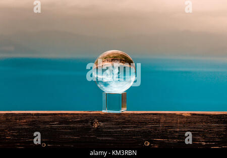 crystal ball on a bench on the edge of a cliff with colorful scenery on the background sea and clouds  greece december Stock Photo