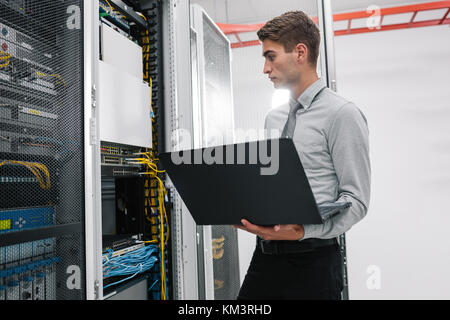 Portrait of modern young man holding laptop standing in server room working with supercomputer Stock Photo