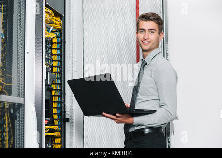 Portrait of modern young man holding laptop standing in server room working with supercomputer Stock Photo