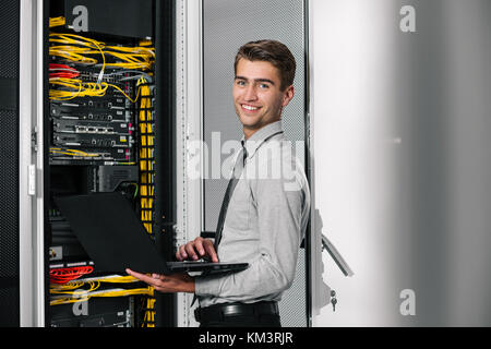Portrait of modern young man holding laptop standing in server room working with supercomputer Stock Photo