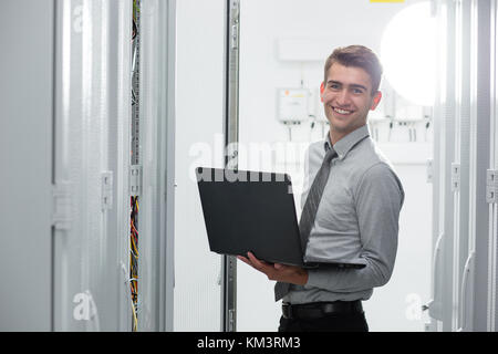 Portrait of modern young man holding laptop standing in server room working with supercomputer Stock Photo