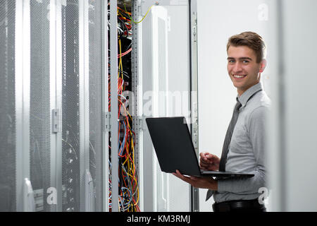 Portrait of modern young man holding laptop standing in server room working with supercomputer Stock Photo