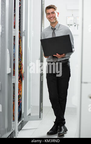 Portrait of modern young man holding laptop standing in server room working with supercomputer Stock Photo