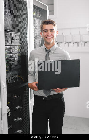 Portrait of modern young man holding laptop standing in server room working with supercomputer Stock Photo