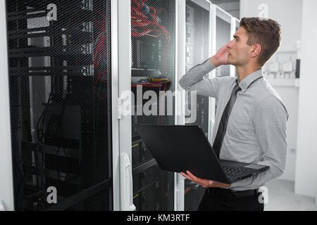 Portrait of modern young man holding laptop standing in server room working with supercomputer Stock Photo
